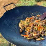 A wok with meat and vegetables on it.