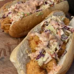 Two hot dogs with coleslaw and a sauce on top.