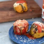 Two stuffed peppers on a plate with sauce.