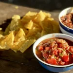 A bowl of salsa next to some chips.