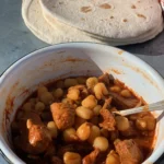 A bowl of stew with beans and tortillas