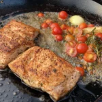 A pan with some meat and vegetables cooking on it