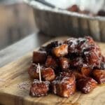 A wooden cutting board topped with meat covered in sauce.