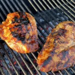 Two chicken breasts are cooking on a grill.