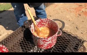 A pot of soup on the grill with a wooden spoon.