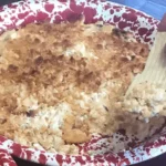 A bowl of rice and meat with a wooden spoon.