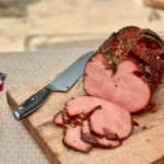 A cutting board with ham and knife on it.