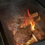 A grill with some meat on it and flames coming out of the grill.