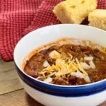 A bowl of chili with cheese and onions.