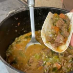 A person is stirring soup in a pot.