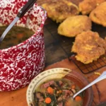 A bowl of soup and some fried food on the table.