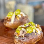 Two baked potatoes with toppings on a wooden board.