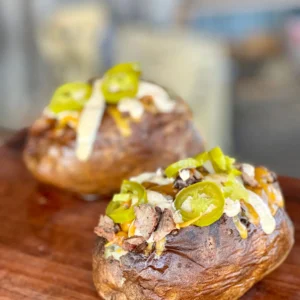 Two baked potatoes with toppings on a wooden board.