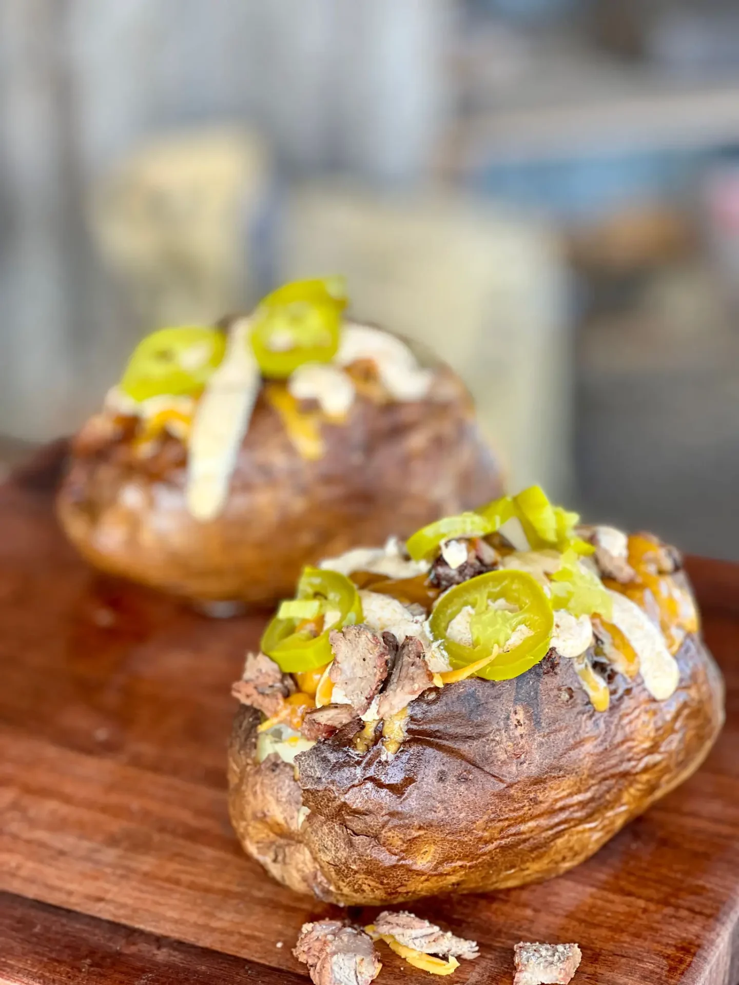 Two baked potatoes with toppings on a wooden board.