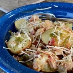 A blue bowl of food with cheese and tomatoes.