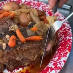 A person cutting up meat on top of a plate.