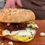 A hamburger with an egg on it sitting on top of a wooden board.