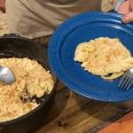 A person holding a fork and spoon over food.