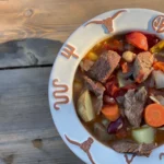 A bowl of stew with meat and vegetables on top.