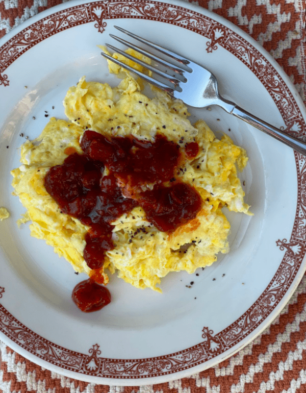 Scrambled eggs with red sauce on a plate.