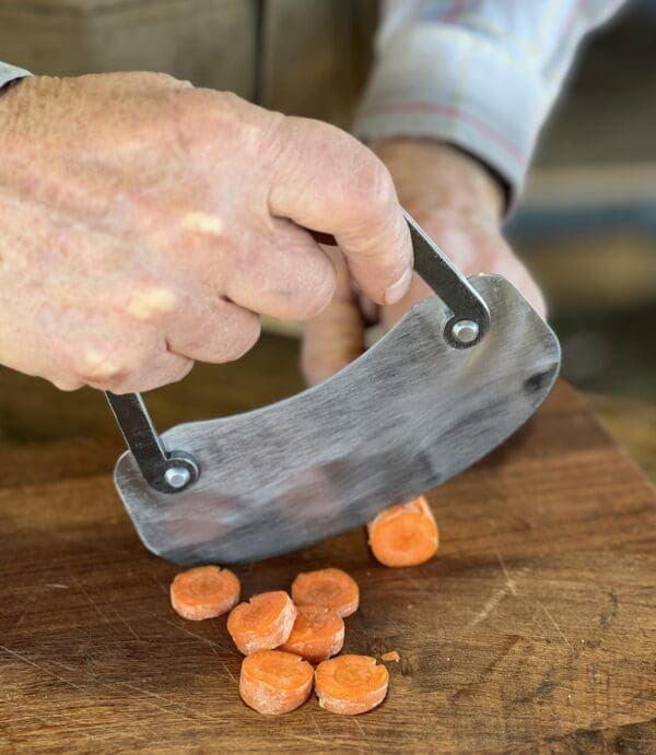 Hand using a knife to slice carrots.