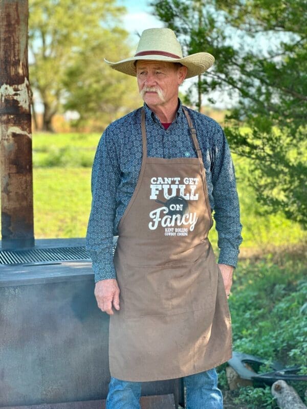 Man in a hat and apron by a grill.