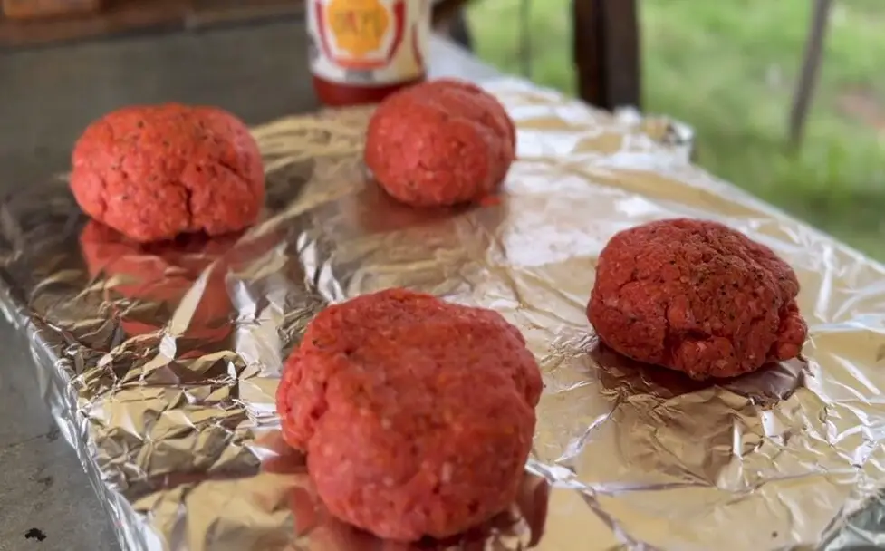 Four baseball sized balls of ground meat atop a sheet of tin foil.
