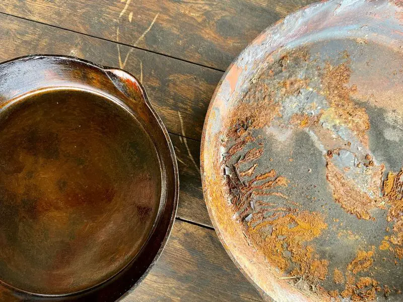 Two cast iron skillets, side by side. The one on the left has been restored after a fire and is a shiny bronze, the one on the right has been has been burned in a fire and is rusted with cracked seasoning, although the skillet itself is sound.