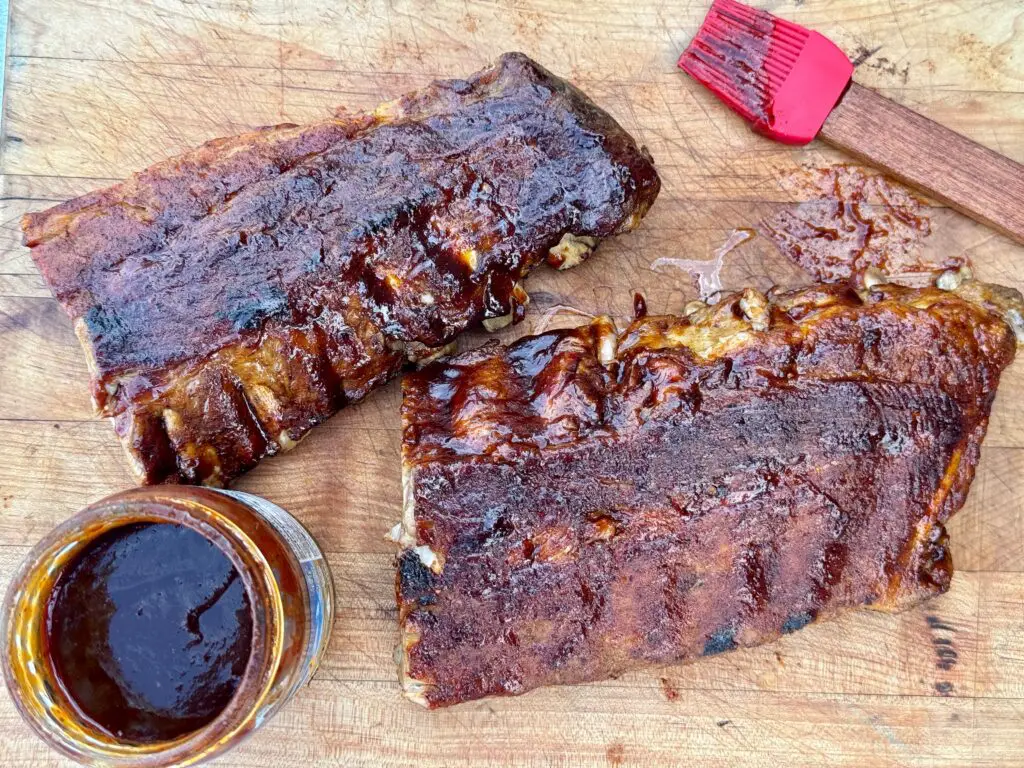 Kent Rollins' Favorite Ribs -no smoker required- on a cutting board with a bowl of bbq sauce and a basting brush.