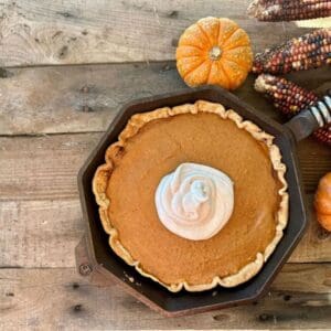 Kent Rollins Sweet Potato Pie Recipe - a cast iron skillet rests on a picnic table near pumpkins and fall colored leaves.