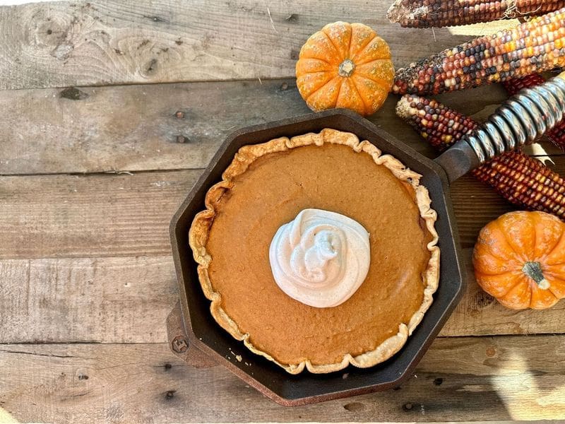 Kent Rollins Sweet Potato Pie Recipe - a cast iron skillet rests on a picnic table near pumpkins and fall colored leaves.