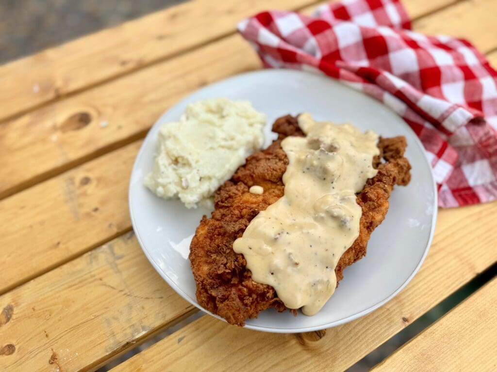 Cowboy Kent Rollins' Chicken Fried Chicken on a white plate, smothered in white gravy with mashed 'taters 