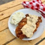 Cowboy Kent Rollins' Chicken Fried Chicken on a white plate, smothered in white gravy with mashed 'taters