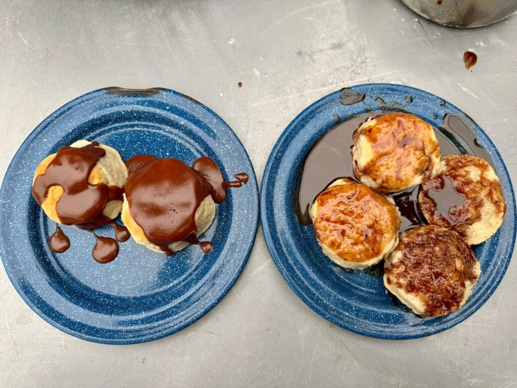 Two blue plates side by side; the left has two biscuits covered in chocolate gravy and the right has two open biscuits covered in chocolate syrup. 