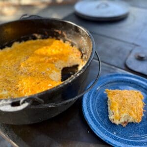 A Dutch oven featuring a delicious hash brown casserole with a piece of casserole on a blue plate
