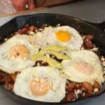 Cowboy kent Rollins' Mexican Hash in a cast iron skillet with four eggs atop potatos, onions, and peppers.