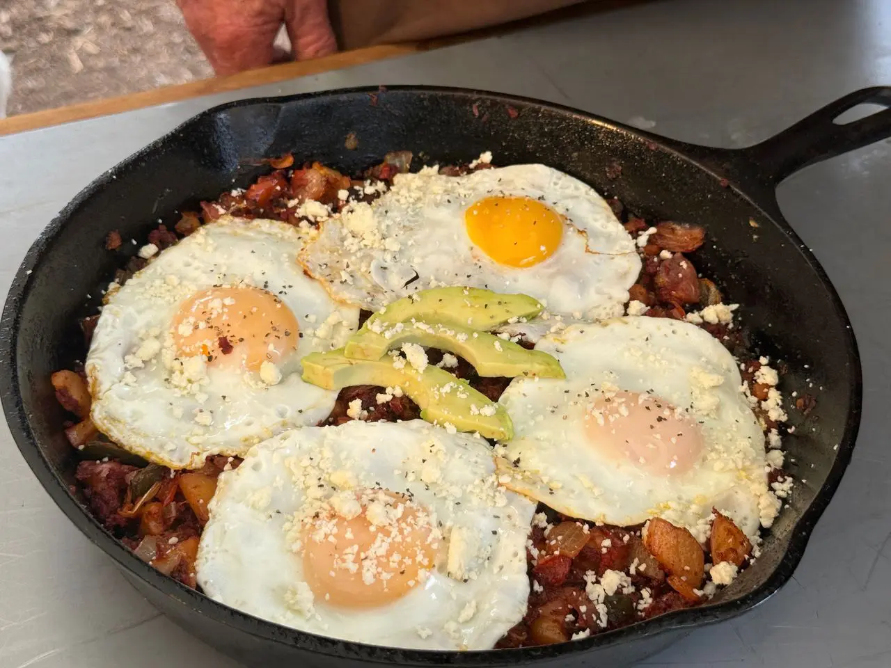 Cowboy kent Rollins' Mexican Hash in a cast iron skillet with four eggs atop potatos, onions, and peppers.