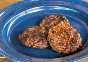 A blue enamel plate containing three perfectly cooked homemade sausage patties, browned to perfection.