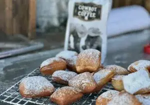 A photo of Kent Rollin's Cowboy Coffee next to a wire rack covered in golden beignets covered with powdered sugar.