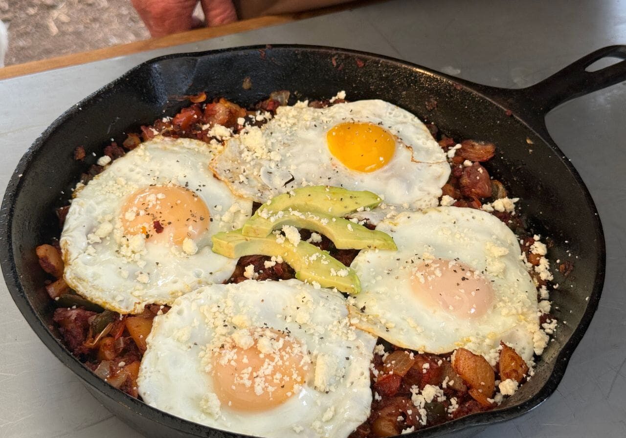 Cowboy kent Rollins' Mexican Hash in a cast iron skillet with four eggs atop potatos, onions, and peppers.